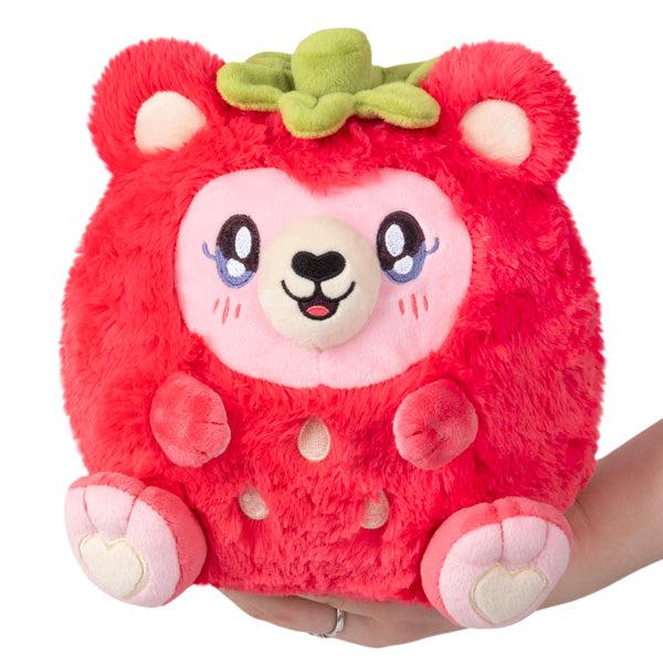 A hand holding a red, plush srawbeary with heart-shaped accents on its paws and a green top resembling a strawberry leaf.
