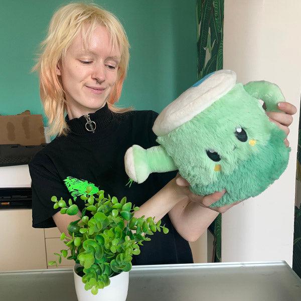 Scene of a woman pretending to water a plant with the plush.