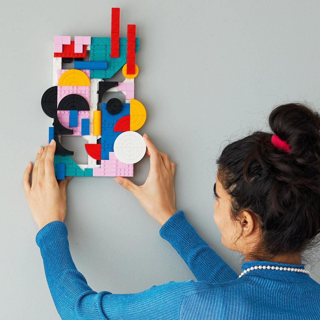 image shows a woman putting the LEGO modern art on a wall