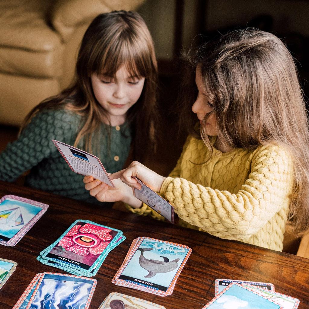 two younge girls are looking at flash cards laid out to learn about animals, and life science at a young age. 