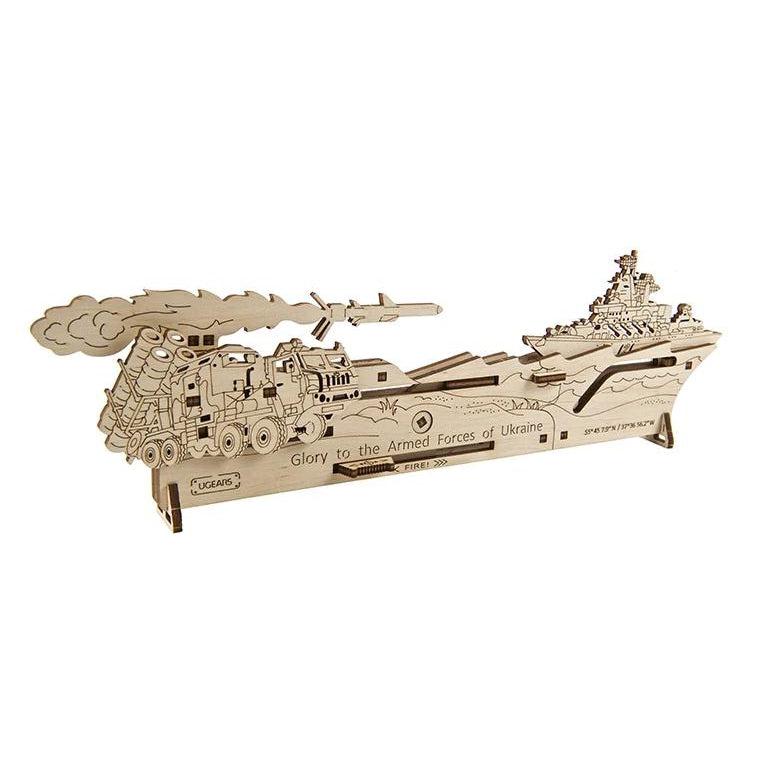 Image of the Neptune Mission model. It is made from unpainted wood and it has a detailed scene of ground forces shooting missiles at an aircraft carrier. On the front are the words "Glory to the Armed Forces of Ukraine"
