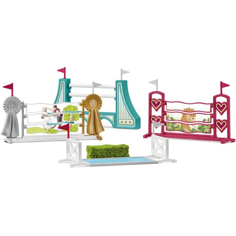 Image of the Obstacle Accessories set. It comes with four different obstacle hurdles. One is blue, one is pink. one is silver and gold, and one is a green bush. Each obstacle has a pink and a white flag marking the obstacle.