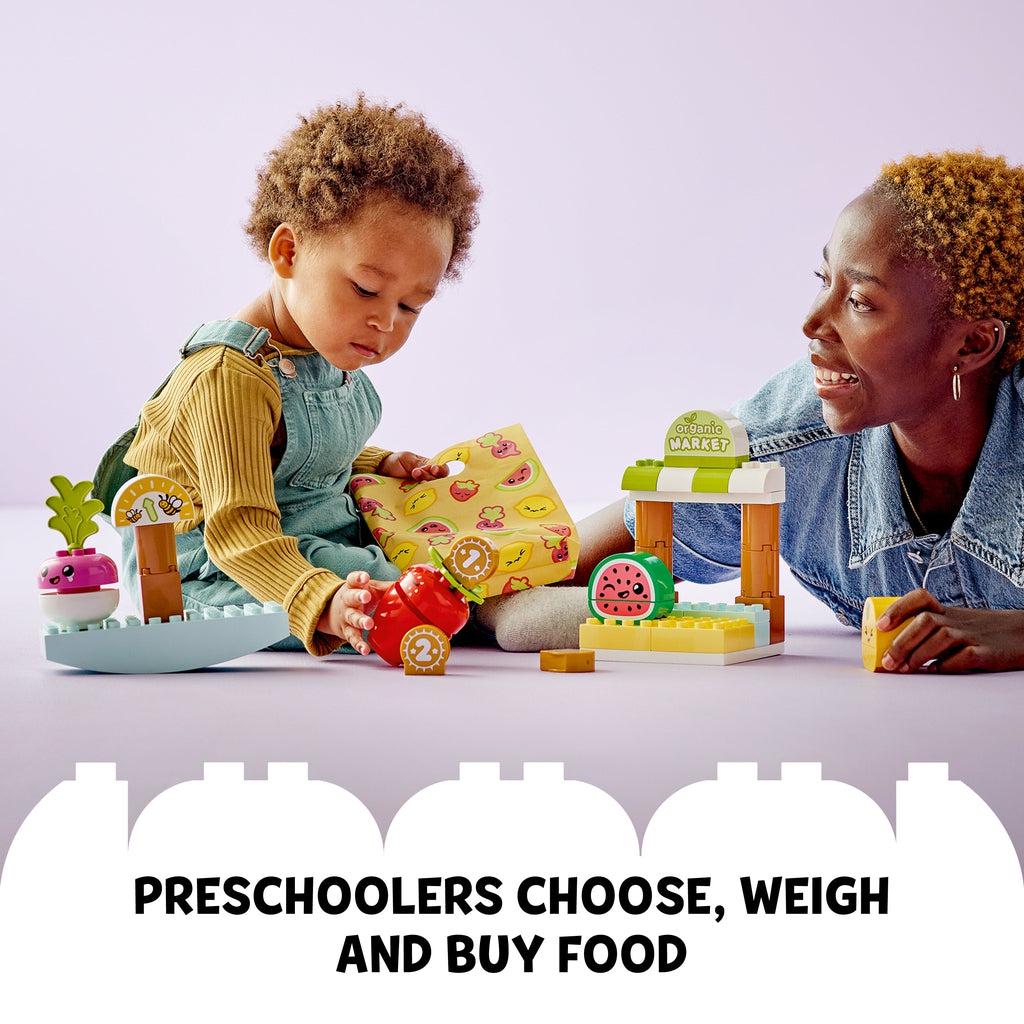 Scene of a mother playing with her son while he plays with the LEGO Duplo playset. Caption: Preschoolers choose, weigh, and buy food