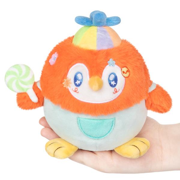 Small orange plush penguin with an adorable face, wearing overalls, a helicopter cap, and holding a lollipop