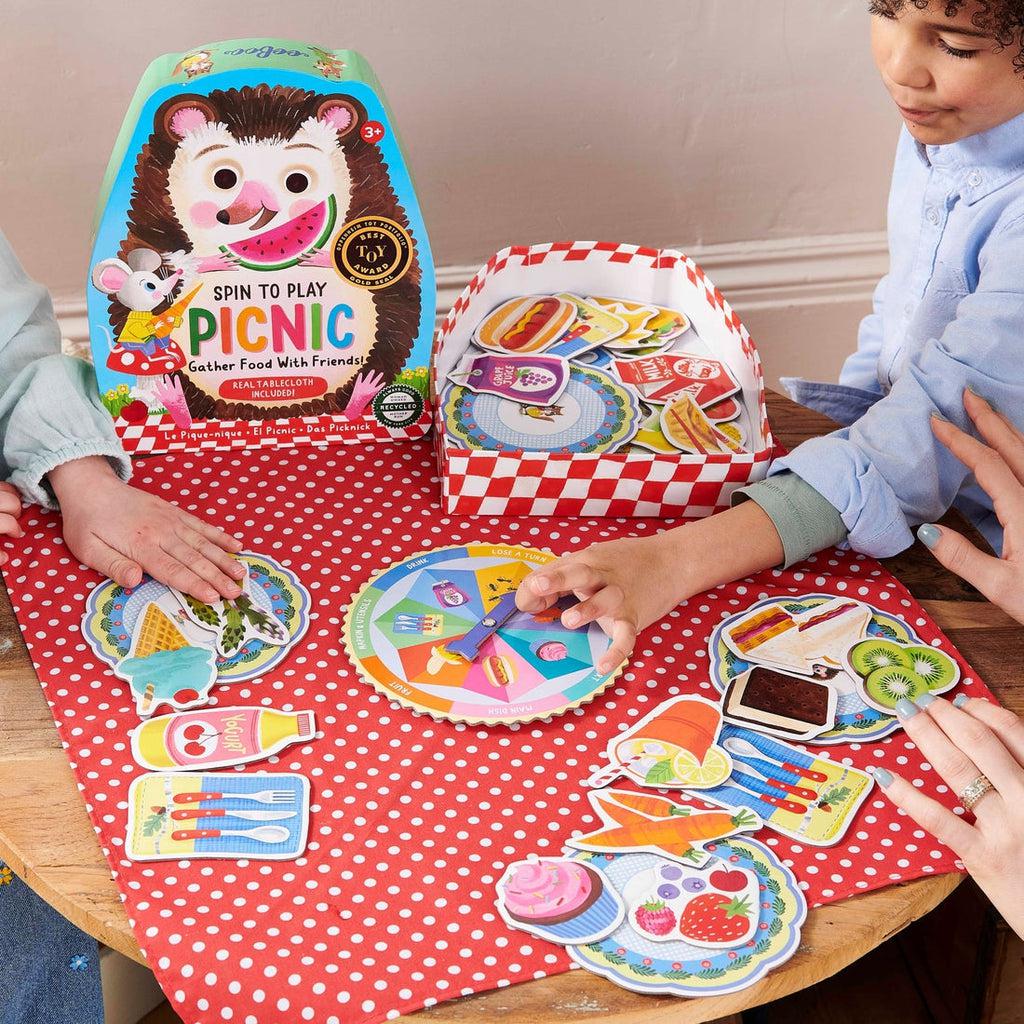 this image shows 3 people playing the picnic game, a kid is spinning th ewheel to see what he can add to his plate
