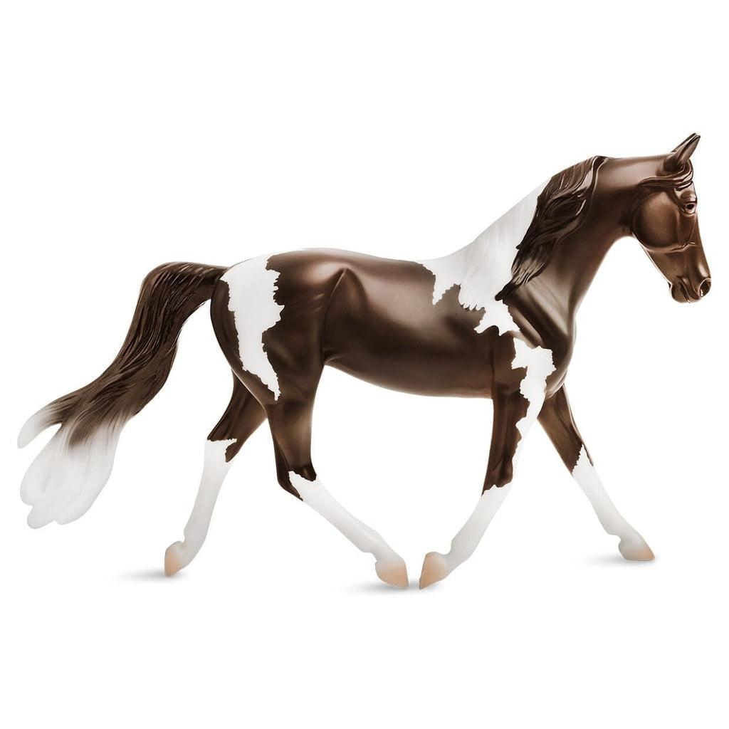 Image of the Pinto figurine. It is a dark chocolate brown horse with many large white spots on its back and white legs.