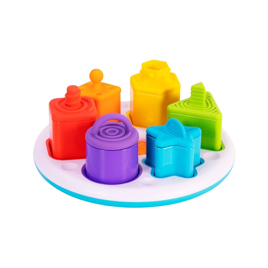 Image of the toy outside of the packaging. It is a base with six differently shaped and colored containers and plugs. It includes a red square, an orange diamond, a yellow hexagon, a green triangle, a blue star, and  a purple circle.