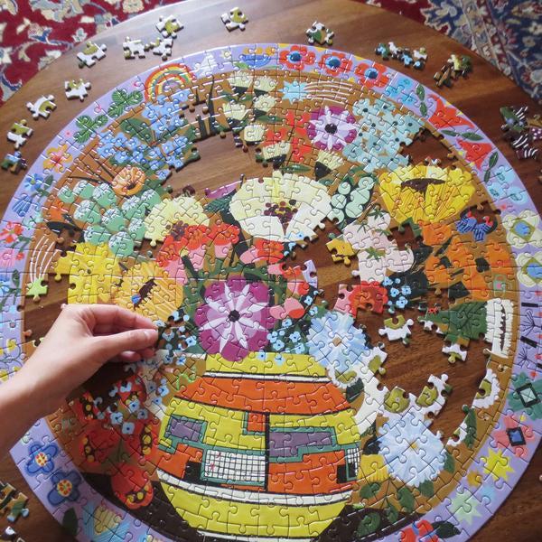 a large tabel is in the background while the puzzle is being completed. there is a vase, and flowers., with a colorful border.