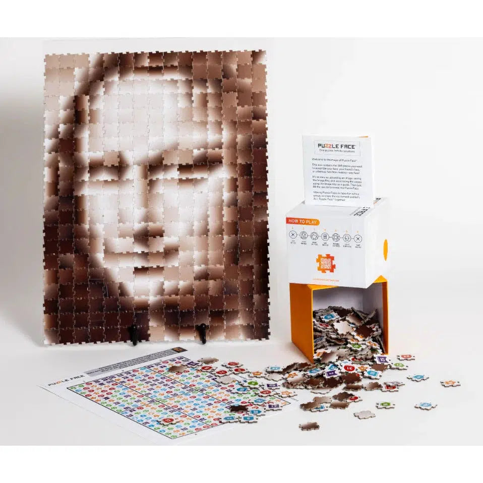 The puzzle face box and pieces on a table next to an image made with them. The puzzle face shows the mona lisa made of squares of shifting tones to form the picture