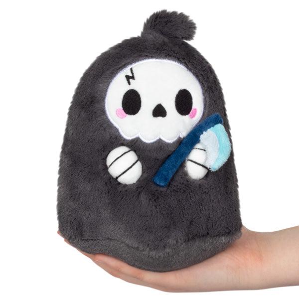 Image of the Reaper Snacker squishable. It is grey and white with a skeleton face. It is holding a blue scythe.