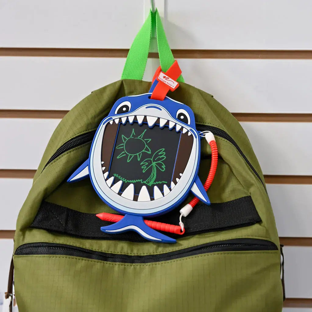the shark is attached to a backpack so a kid can doodle while at school