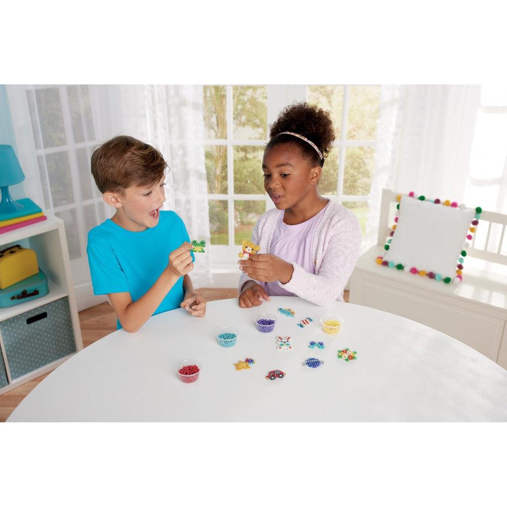 this is an image of two children playing with aquabeads and building something new to play with