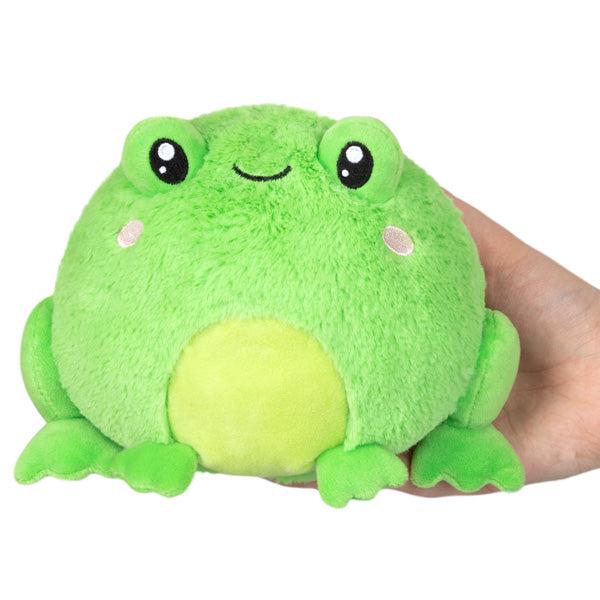 A frog toy plush round and green with large eyes and a smiling face, held in a human hand against a white background.