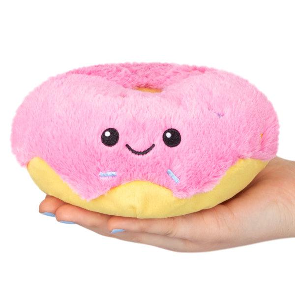 A hand holding a plush toy shaped like a smiling pink donut with sprinkles.