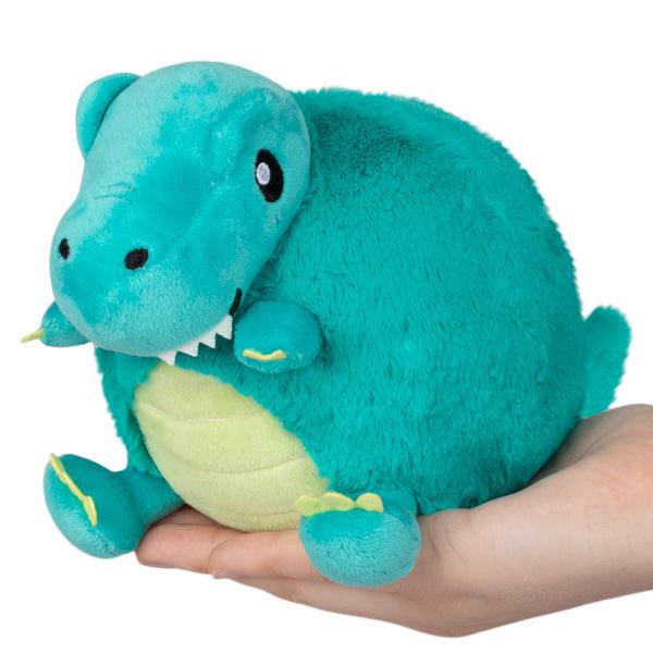 A plush turquoise T-rex dinosaur toy with a rounded body and small limbs, held gently in a person's hands.