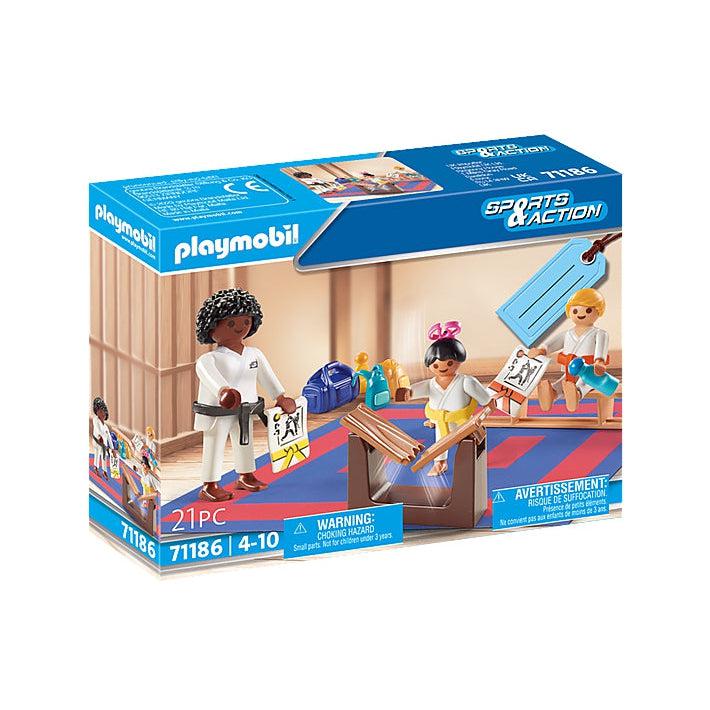 This image shows the box and art cover for the karate playmobi set. There is a teacher and two students practicing karate, one student is delivering a powerful karate chop to a wooden board, breaking it in two. the other student is taking a water break, holding onto his karate certificate.