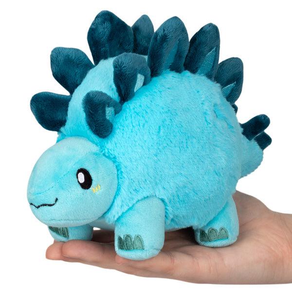 Image of the Stegosaurus Snacker squishable. It is a light blue with darker blue spikes on its back.