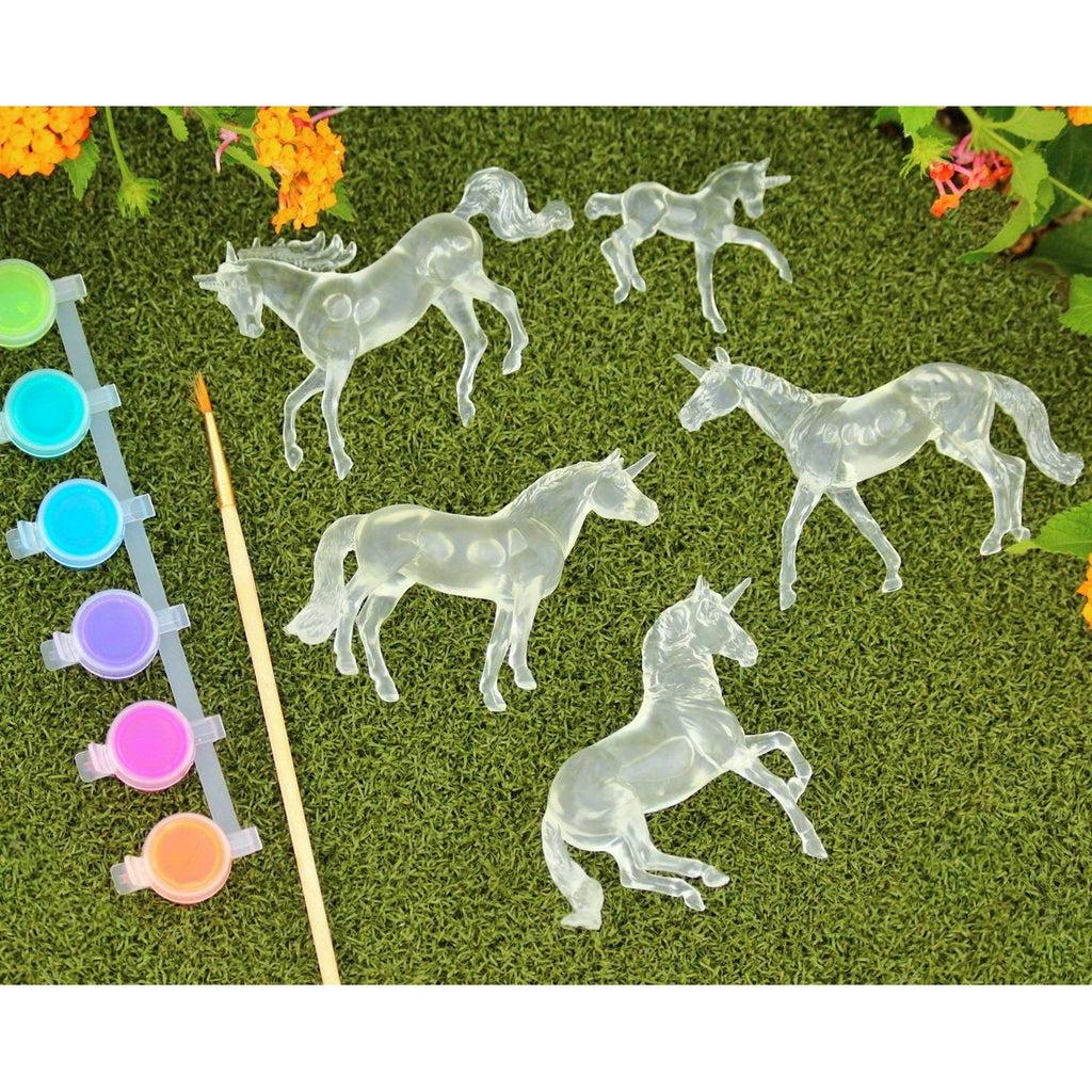 Image of all the included craft materials. It comes with five different clear unicorn figures, a 6 color paint set, and a paintbrush.