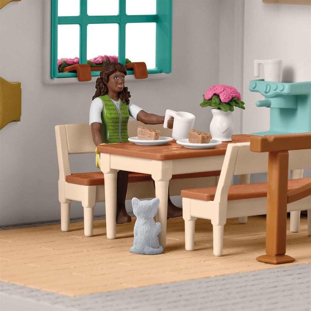 The girl figurine is shown sitting at a table and holding a mug in one hand