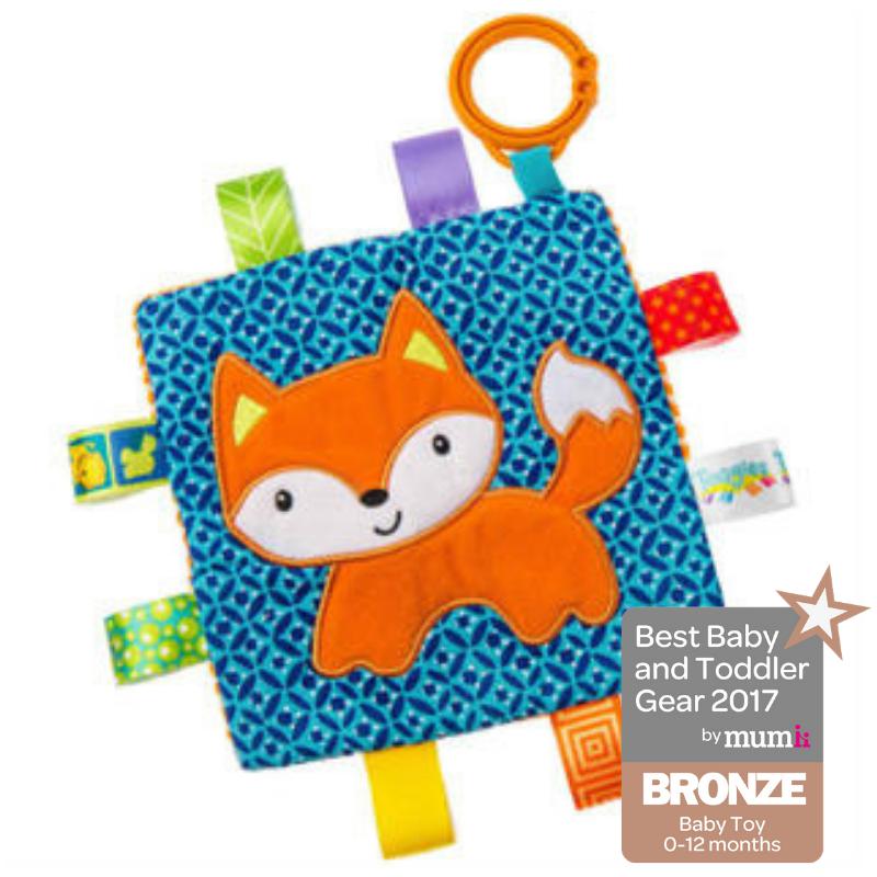 Image of the Taggies Crinkle Me Fox. On the front is an embroidered smiling fox against a blue patterned background.. On the edges are ribbon tags made from fabrics that fit the color theme.