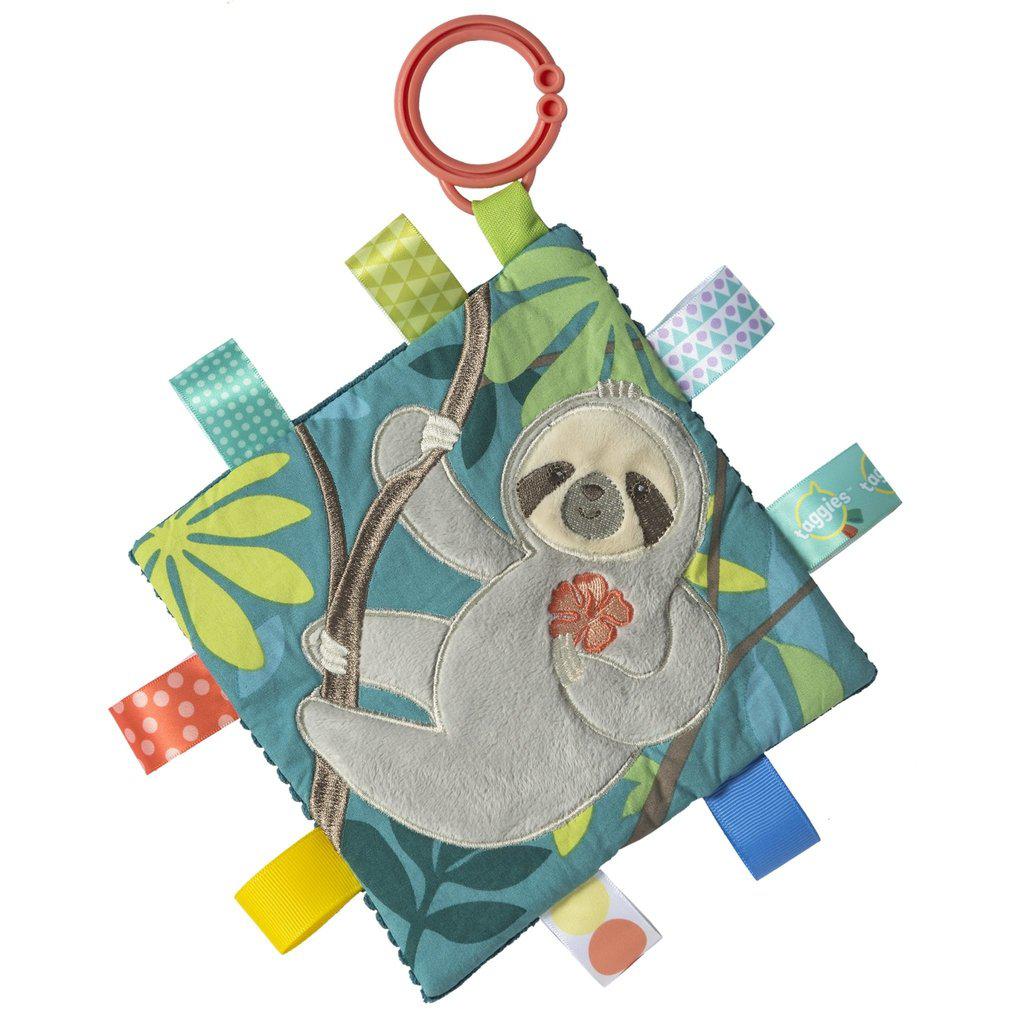 Image of the Taggies Crinkle Me Molasses Sloth. On the front is an embroidered sloth in a jungle hanging from a tree. On the edges are ribbon tags made from fabrics that fit the color theme.