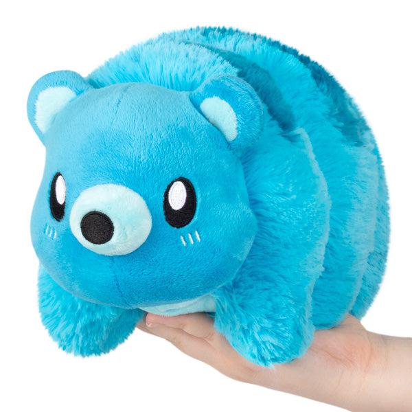 A hand holding a blue Tardigrade plush with an adorable face, isolated on a white background.