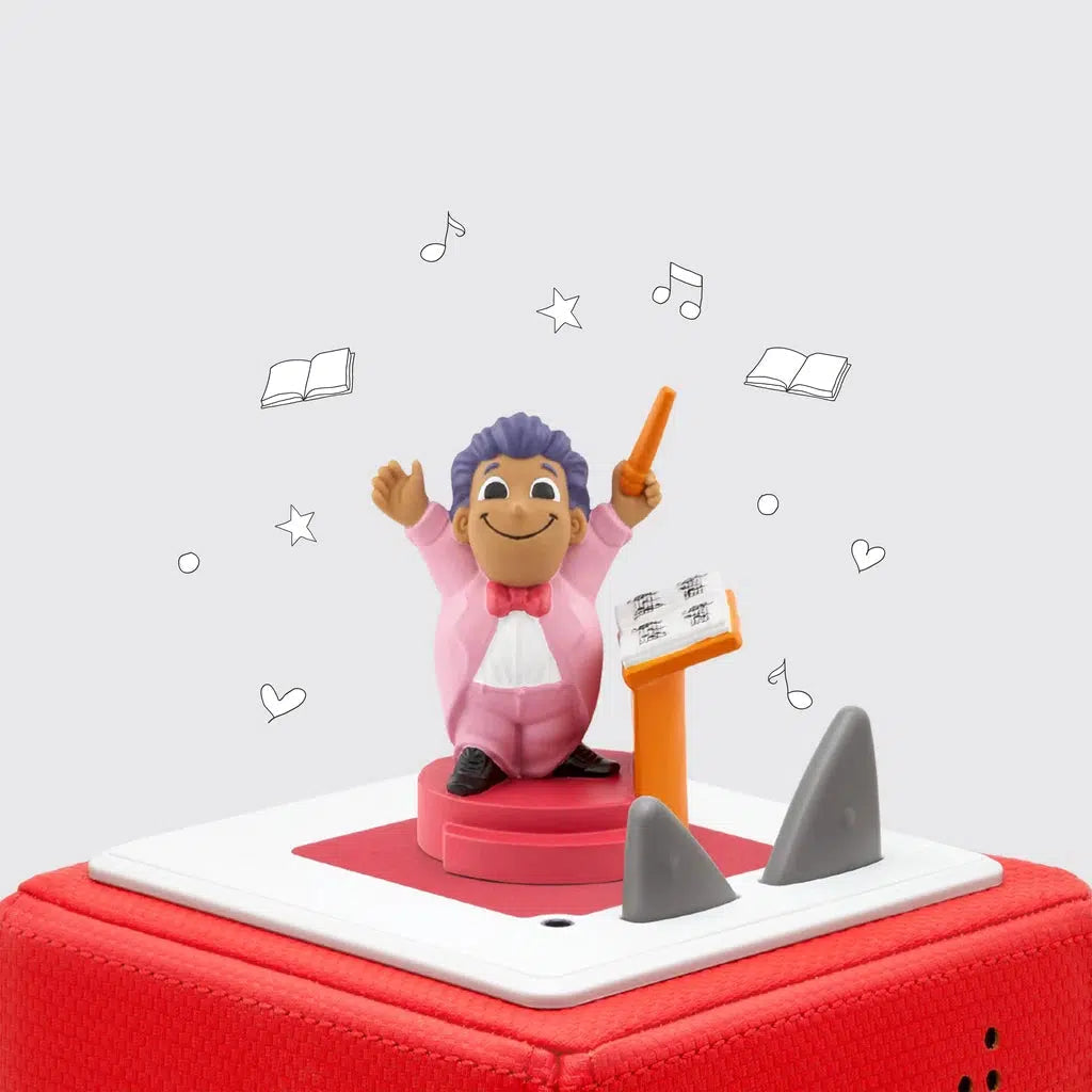 The tonie figure is shown on a toniebox. The figure is a cartoonish man in a pink conductors suit and white shirt with a red bowtie. He's holding a conductors baton into the air and is next to a music stand.