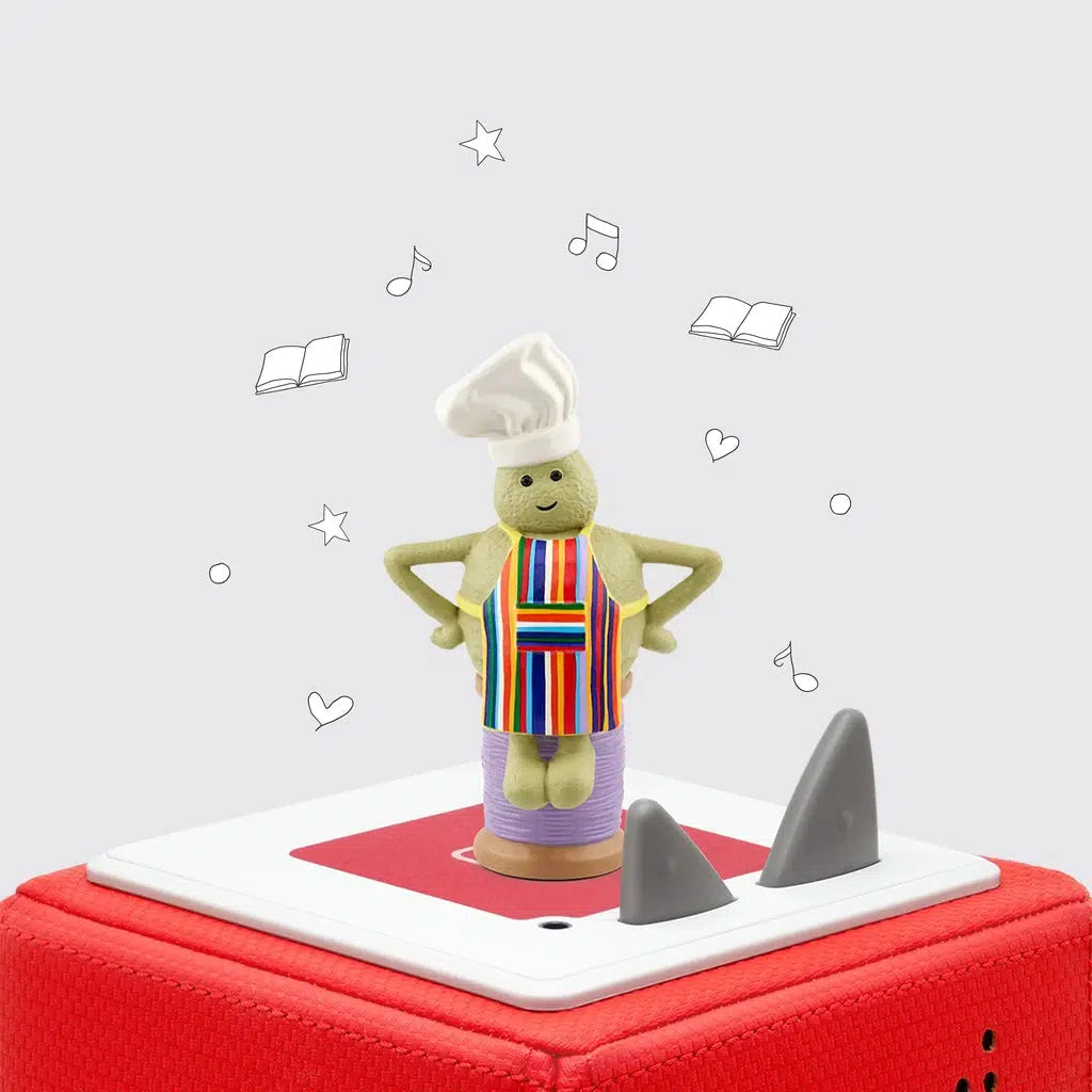 The tonie figure is shown on a toniebox. The figure is a small green man who looks to be made of clay. He's wearing a white chefs hat and a striped apron of various colors, he's also sitting on a spool of purple thread.
