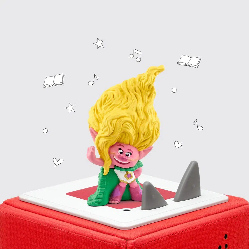 The tonie figure is shown on a toniebox. The figure is the character "Viva" from trolls, a pink troll with a large mess of yellow hair, and a green cape.