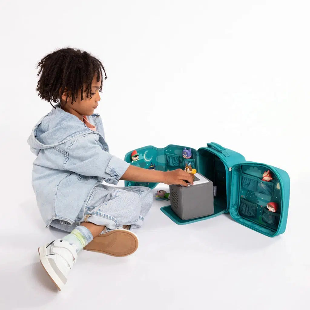 child playing with the case with the toniebox on the fold down placemat in the process of placing a tonie figure on top