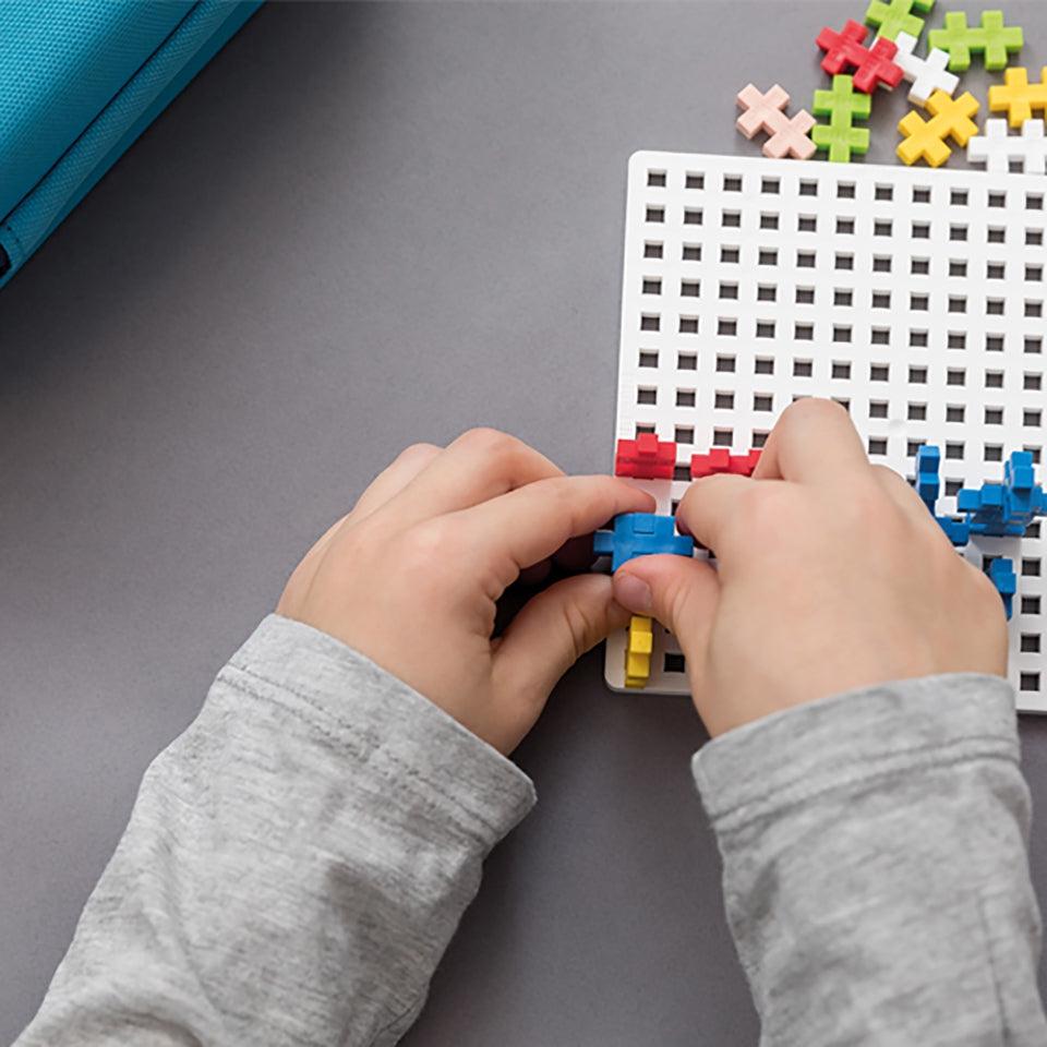 a kid is putting colored bricks on a white board with holes for the Plus shaped bricks