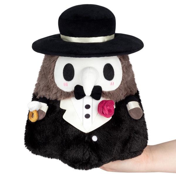 A mini squishable plush toy of a plague doctor, dressed in a tuxedo and top hat, held in a person's hand against a white background.