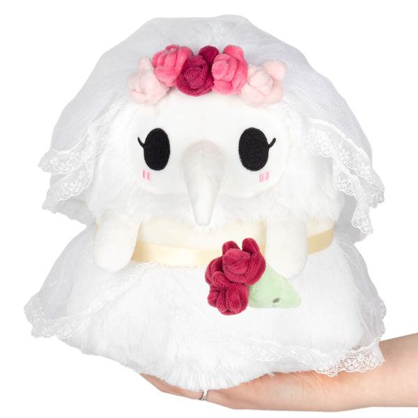 A plush plague nurse dressed in a white bridal veil and dress, decorated with pink rose accents, held in a person's hand 