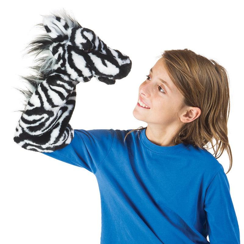 Child looks at zebra puppet on hand.