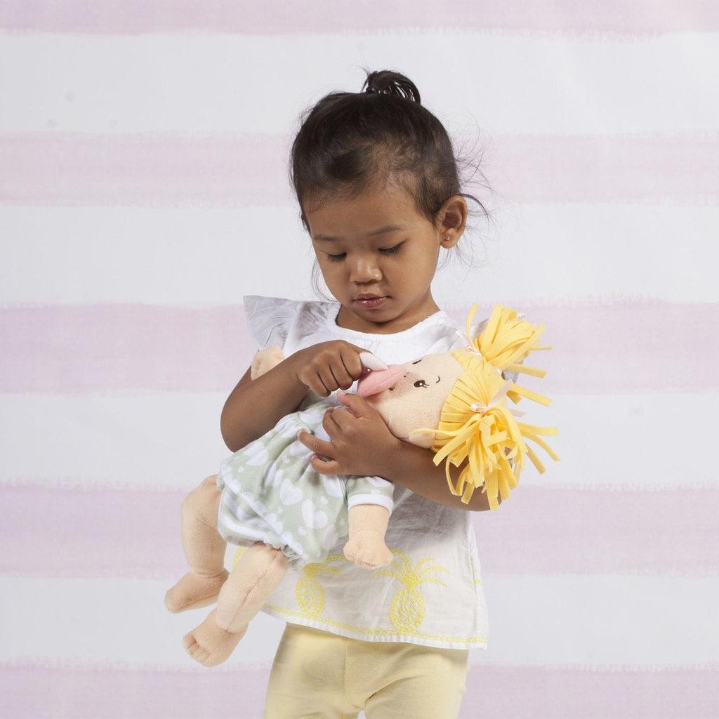 A child is holding the baby stella doll in her arms, and is putting the pacifier on the dolls mouth.