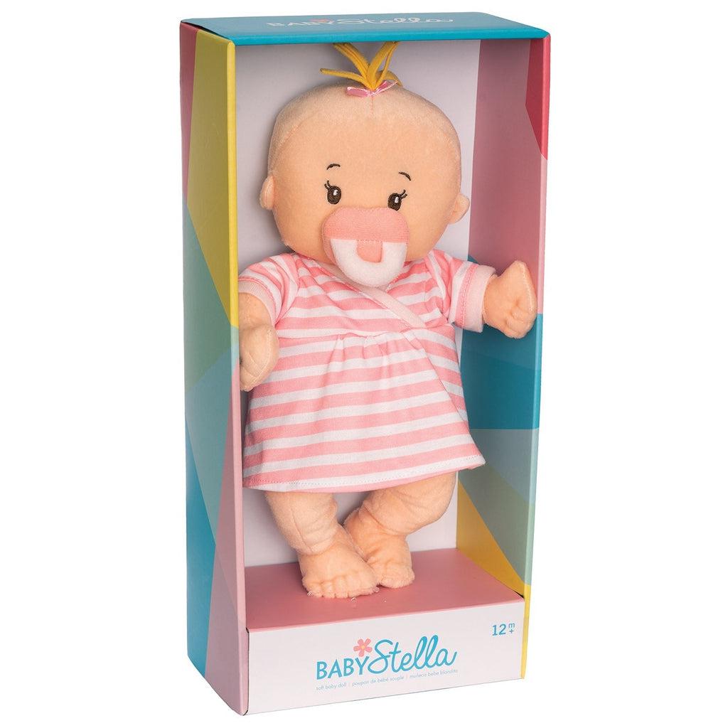 A baby doll is in a box that reads: "baby stella" at the bottom. The doll has a pacifier, a pink and white stripped dress, and a tuft of hair at the top of its head.