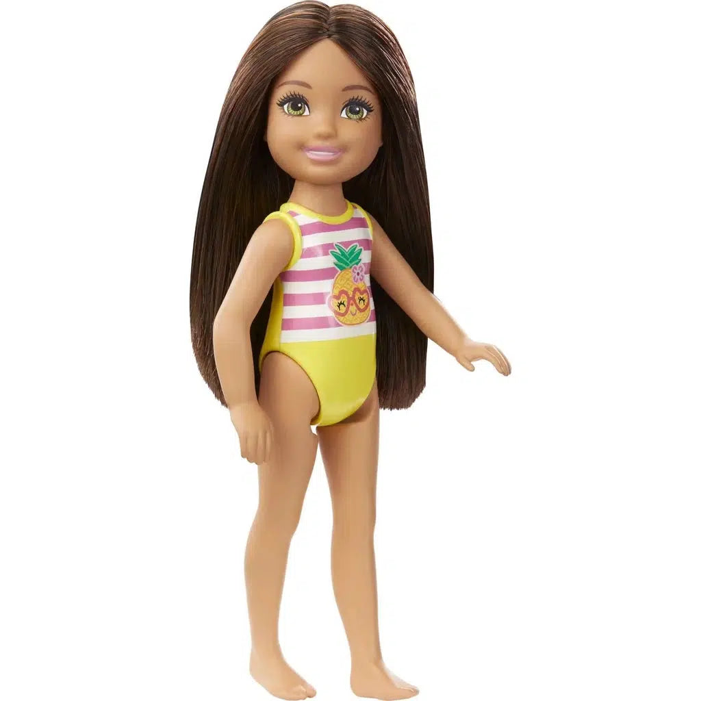 The Chelsea doll out of the box. it has brown hair down to the waist and a yellow one piece swim suit with pink stripes and a graphic of a pineapple in heart glasses on the front.