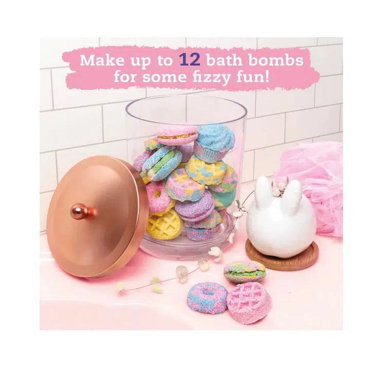 Text reads: Make up to 12 bath bombs for some fizzy fun! Image displays a container filled and surrounded by cupcake, waffle, donut, and macaroon shaped bath bombs, there is also a small bunny shaped plant pot and a luffa next to the container. The image appears to be set on the rim of a bathtub.