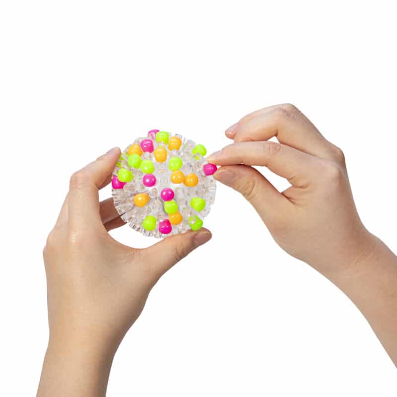 Image shows someone attaching caps the bright ball with a bunch of other caps already attached on various parts of the ball.