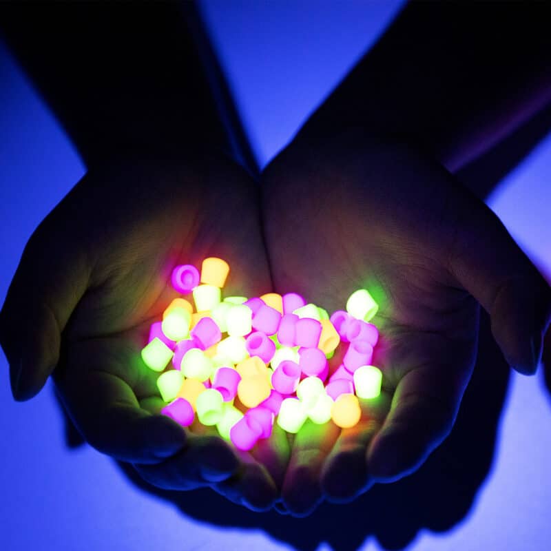 In a dark room a pair of hands holds a pile of the caps with some of each of the three colors. They are all glowing brightly.