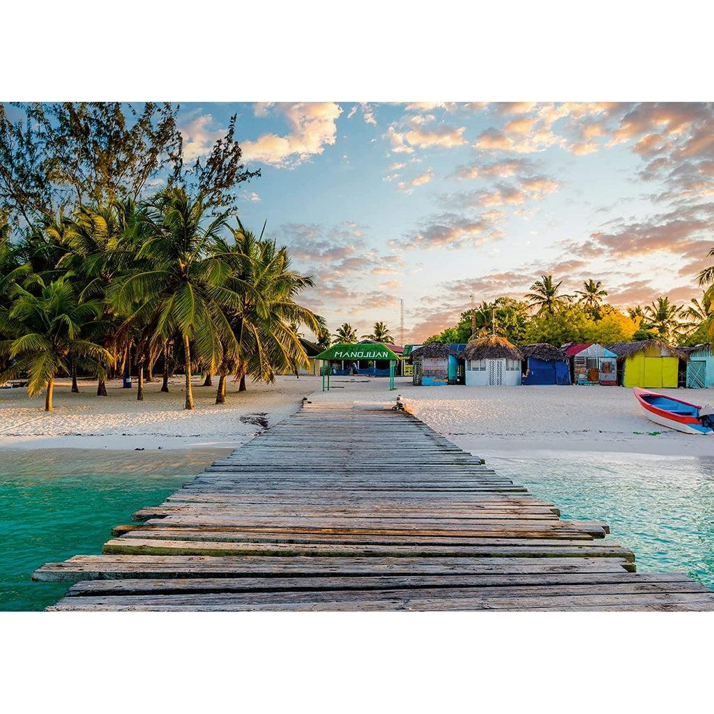 Puzzle image | View of beach as if viewer is standing on an ocean dock | Dock is made of weathered wood with turquoise water on either side and a white sand beach at the end | Beach has a grouping of palm trees and multiple, colorful huts backed by more trees.