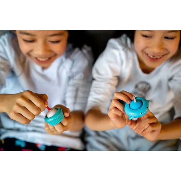 two children are seen smilling and playing with a pull n' pop each. The child on the left is holding the cupcake popper and the one on the right is holding a narwhal popper. Cupcake and Narwhal popper not included in this product, but both are available on the red balloon site.