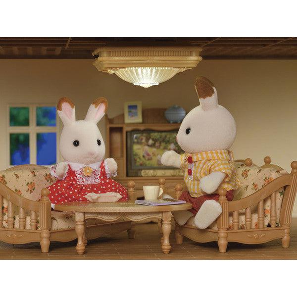 Scene of two well-dressed rabbits sitting at a coffee table with the ceiling light above them.