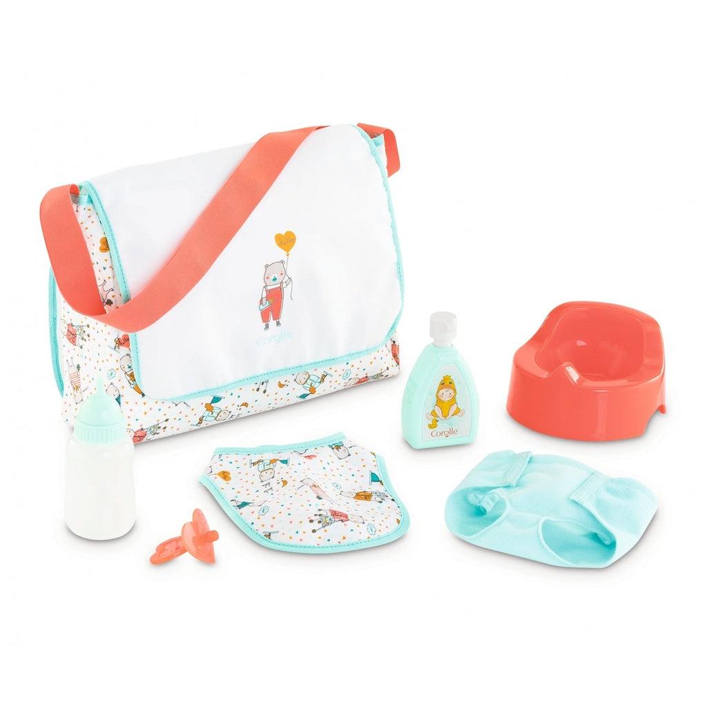 All the items are spread out on a white background. There's a red potty, a blue cloth diaper, a bib with cartoon bear characters on it, a bag with the same pattern on the base and a single cartoon bear on the front of the closure flap. There is also a pacifier, baby powder, and a bottle. All doll sized