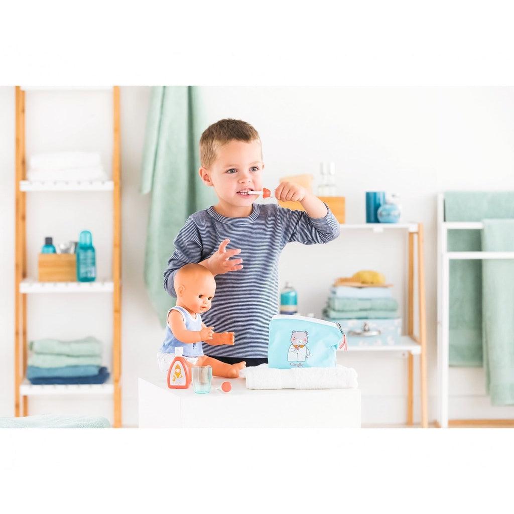 A small boy is shown brushing his teeth next to a baby doll and the care pouch and accessories