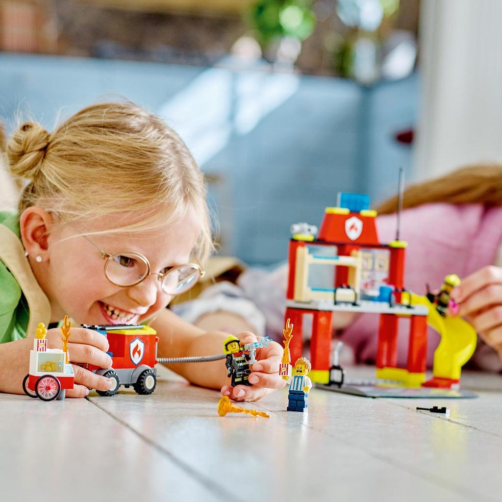 a child is shown playing with the lego set on the floor with another persons hand visible to the right also playing with the set