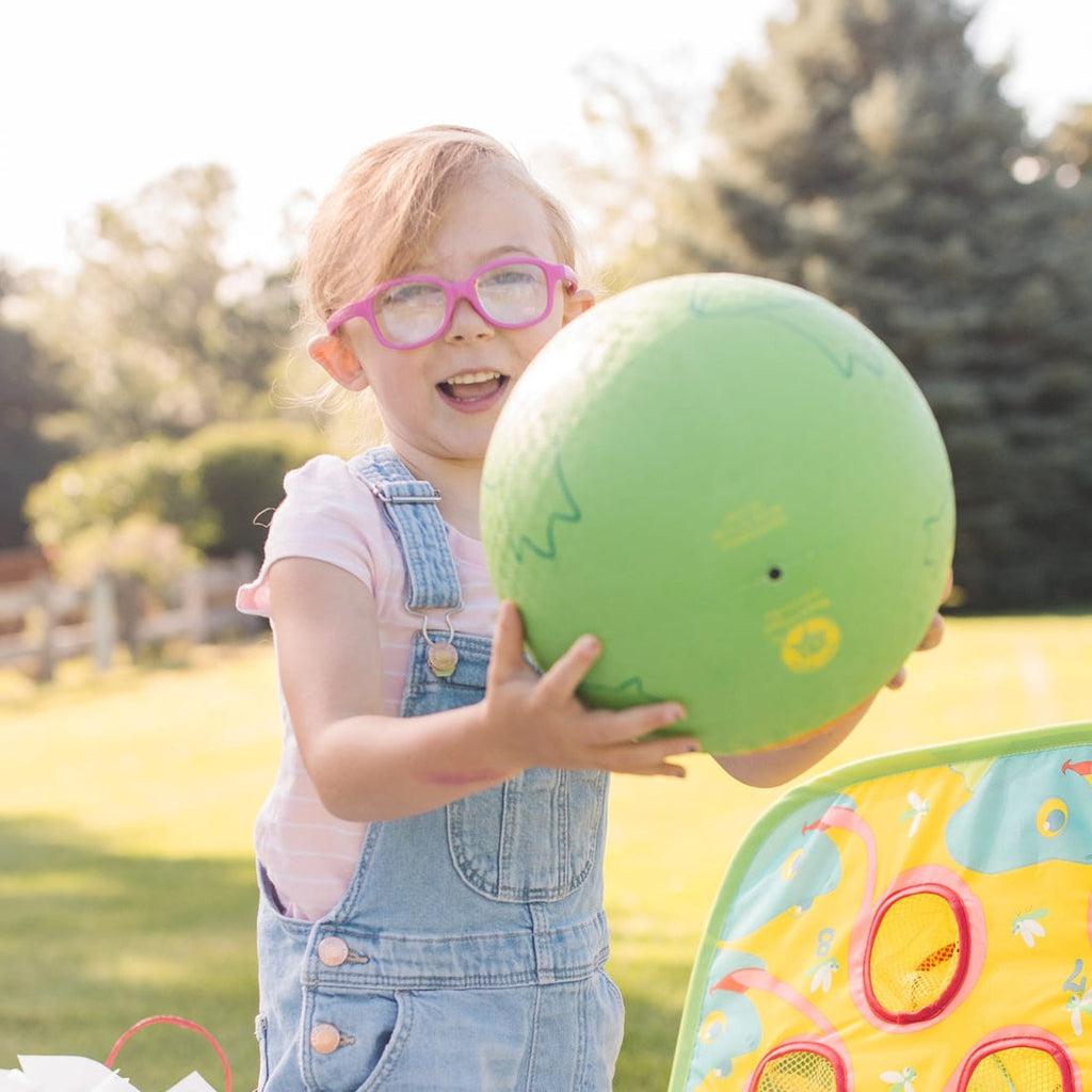 Smiling child holding green frog ball and playing outdoors