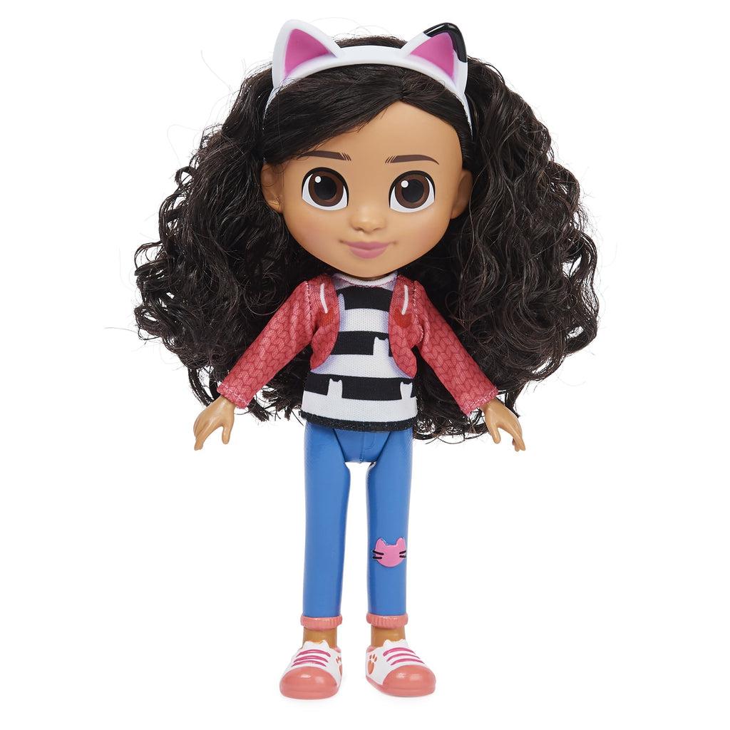 Doll out of packaging | 8 inch tall doll with white and pink sneakers, blue pants, a black/white stripe shirt and pink jacket. She has on a cat ear headband and small cat details through the outfit. She has brown curly hair and brown eyes.