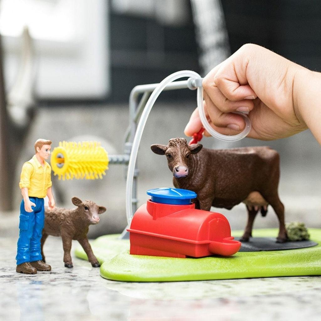 Scene of a little boy playing with the cow wash play set near the sink. He is hosing down the mother cow.