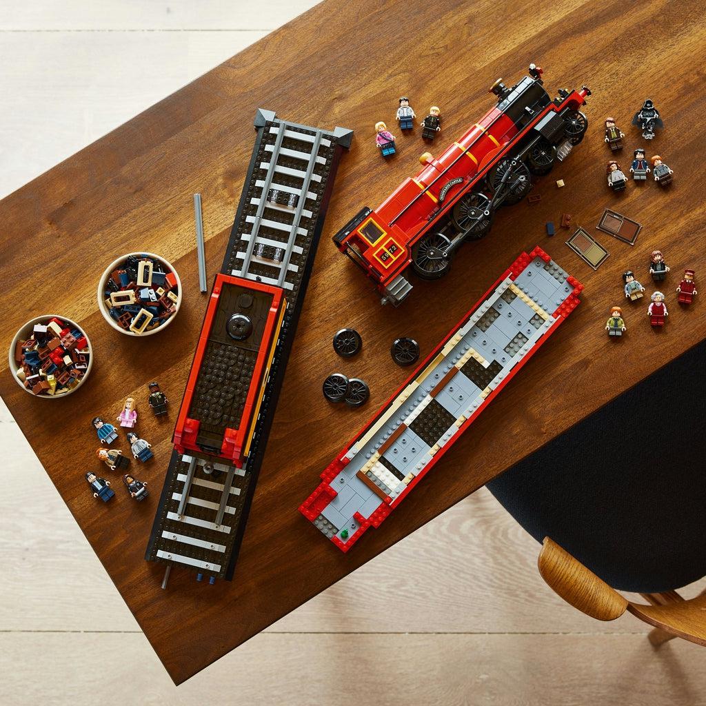 the train is shown with the middle car on the partially built tracks, the engine car is fully built on it's side on the table, and the rear car is half way built on the table. The minifigures are spread all across the table grouped by the movie they are from.